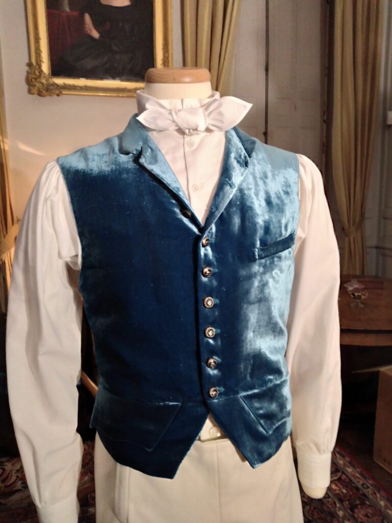 Reconstitution de la tenue de chasse. Vue du gilet en velours turquoise porté sur une chemise blanche avec une cravate nouée blanche autour du cou