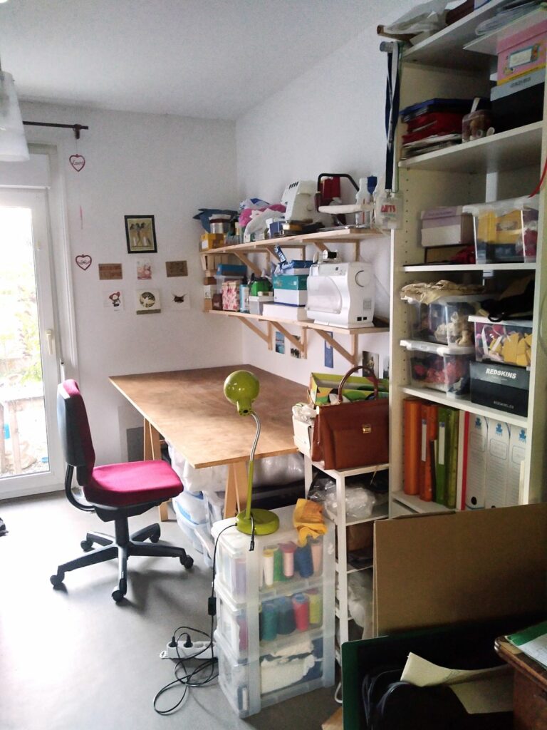 Atelier de couture avec une chaise, une grande table et des étagères avec le matériel