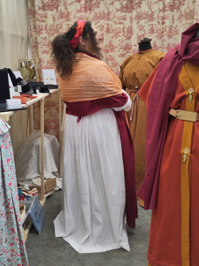 Photo d'Anaïs Mérat portant une robe blanche ceinturée d'un large ruban de velours rouge, avec un châle rouge foncé et un châle orange pâle, vue de dos