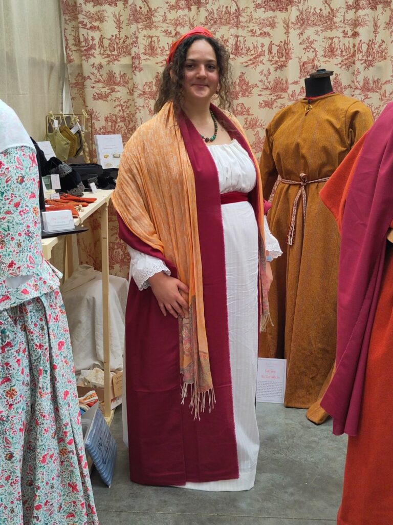 Photo d'Anaïs Mérat portant une robe blanche ceinturée d'un large ruban de velours rouge, avec un châle rouge foncé et un châle orange pâle