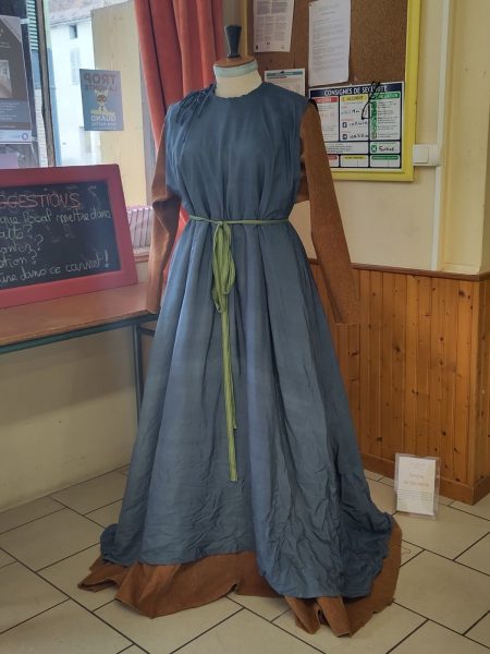 Robe longue et ample orangée sous un surcot bleu, ceinturés par une passementerie verte, portés sur un buste d'exposition