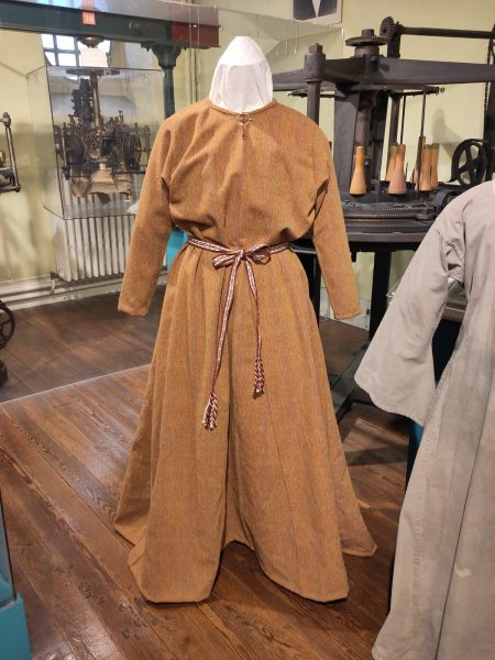 Robe orangée longue et ample avec une ceinture textile rouge, jaune et blanche, fermée par un fermail à l'encolure