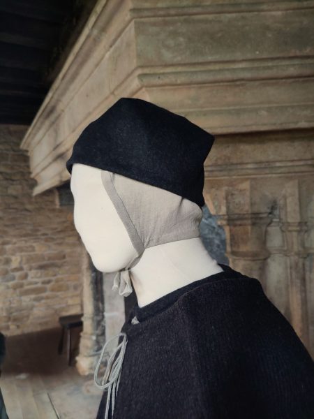 Tête du mannequin habillé d'un bonnet noué sous le menton et d'un petit chapeau gris foncé. Vue de côté